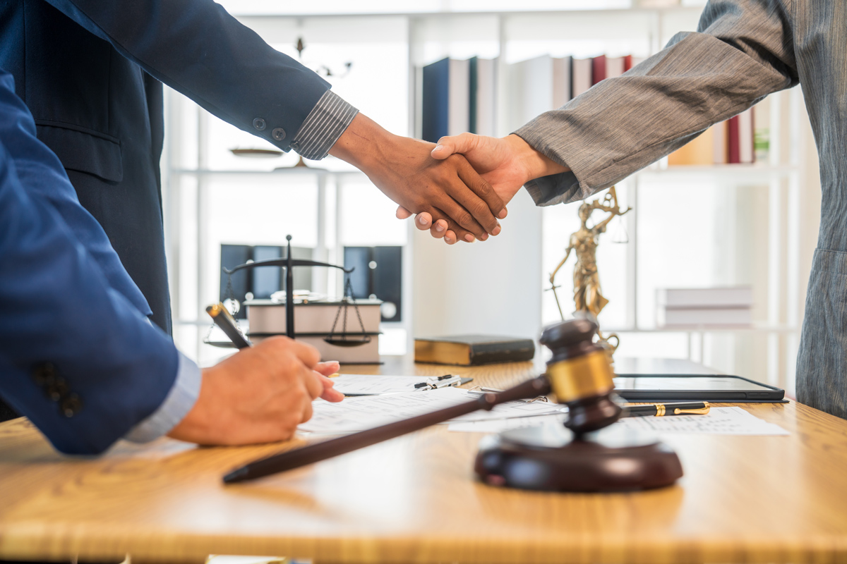 people coming to a settlement, shaking hands over a desk with a gavel.